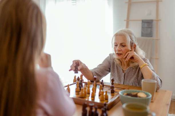 The living room is alive with concentration as a grandmother and granddaughter strategize over a chess board, enjoying their time together.