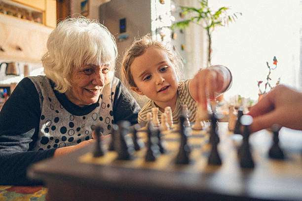 Grandmother and child playing chess board, happy family time.