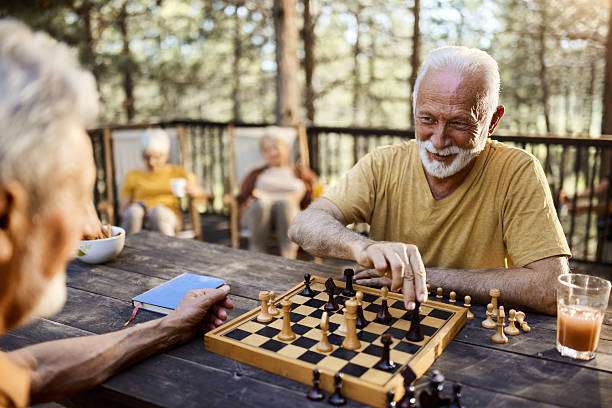 Two smiling senior men playing chess board outdoors on a rustic wooden table.