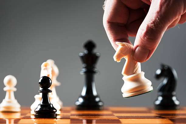 Hand moves white knight chess piece on wood chess board.