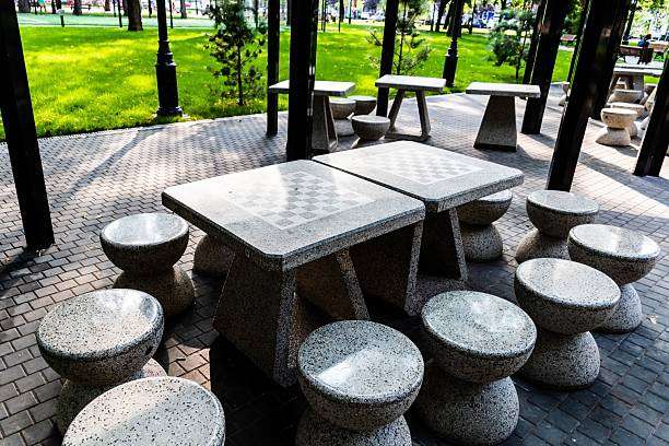 Outdoor park tables with built-in chess board patterns and stools for public play.