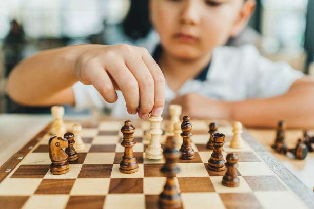 Child's hand moving a white queen on a wooden chess board during a game.