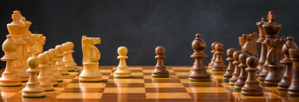 Close-up of a wooden chess board with intricately carved white and black pieces positioned.