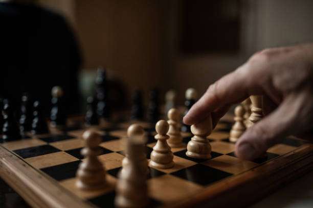Hand moving a pawn on a wooden chess board.