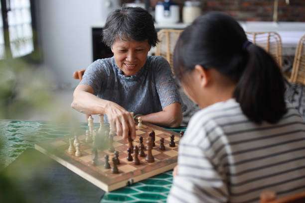 A cheerful Asian grandmother and her granddaughter are playing a game of chess board