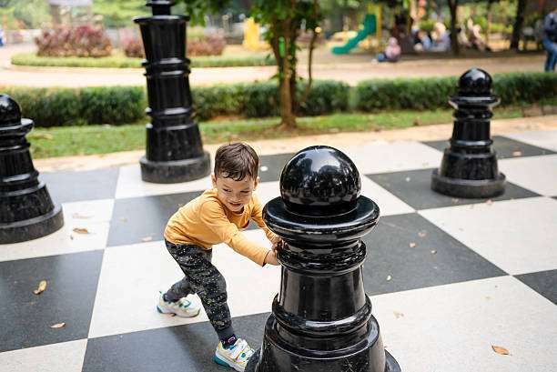 Boy plays with large chess pieces on outdoor chessboard