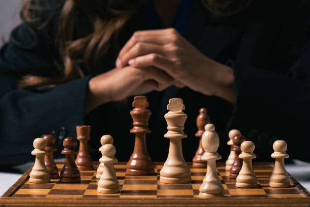 Businesswoman with hands clasped making decisions with a calm and collected demeanor in front of chess board.