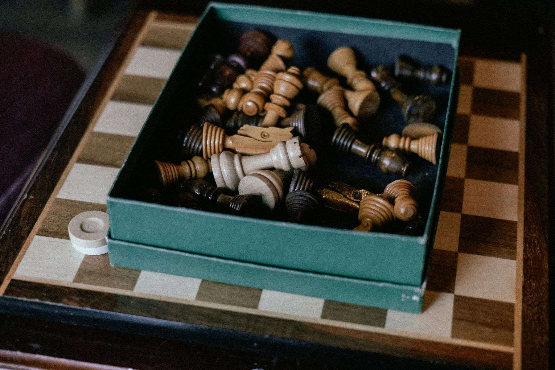 Chess pieces stored together in a box beside a wooden board